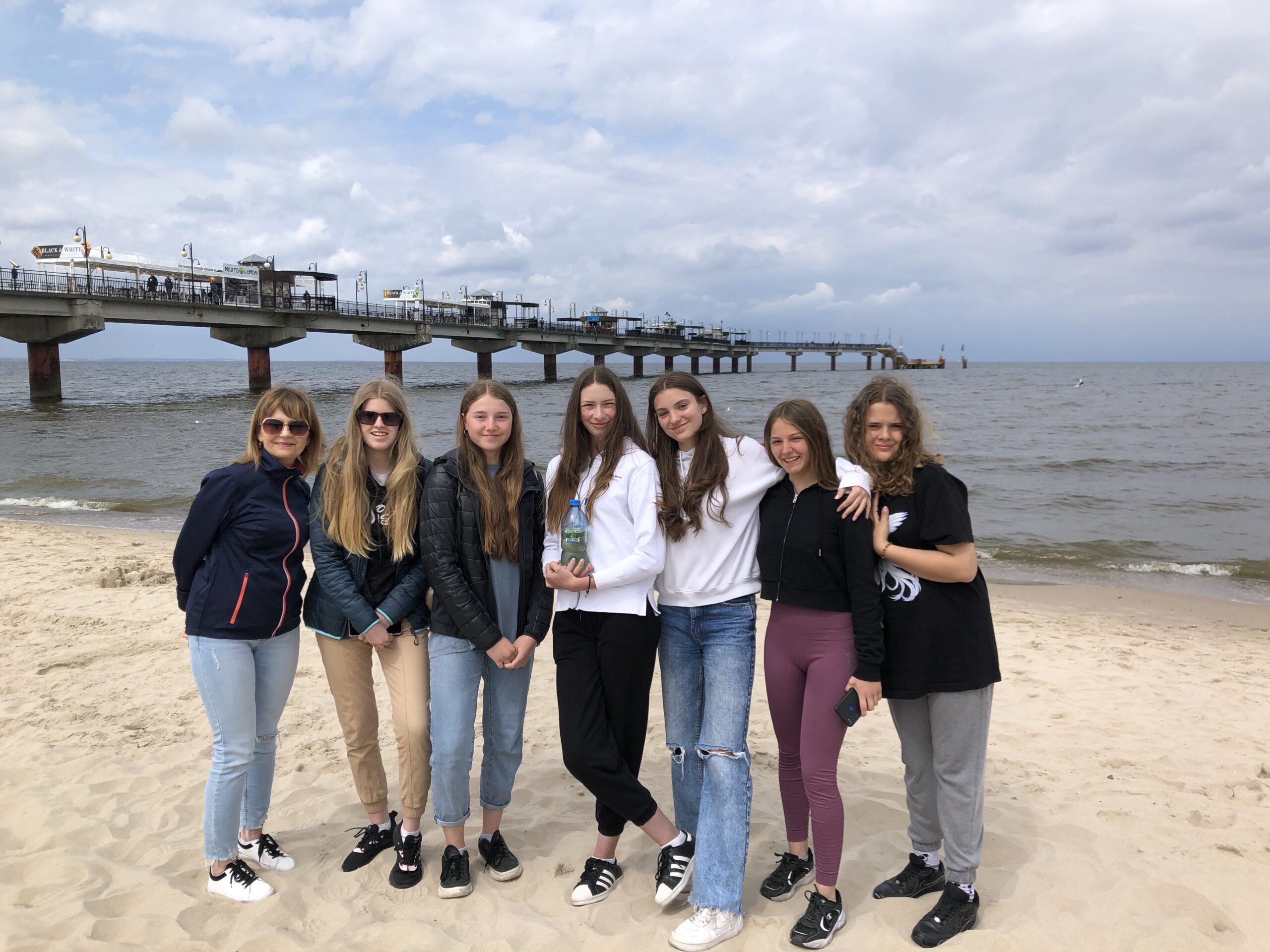 Siedem dziewcząt pozuje na plaży na tle mola