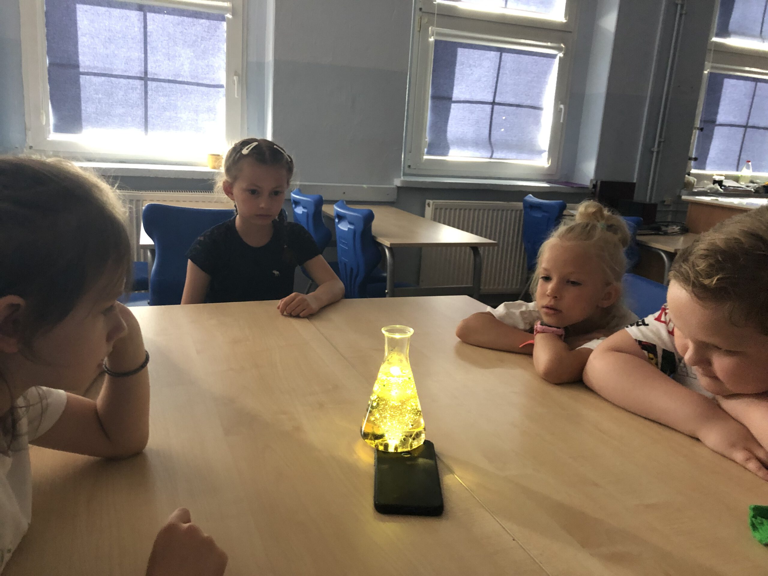 Czwórka dzieci przygląda się kolbie z żółtym płynem