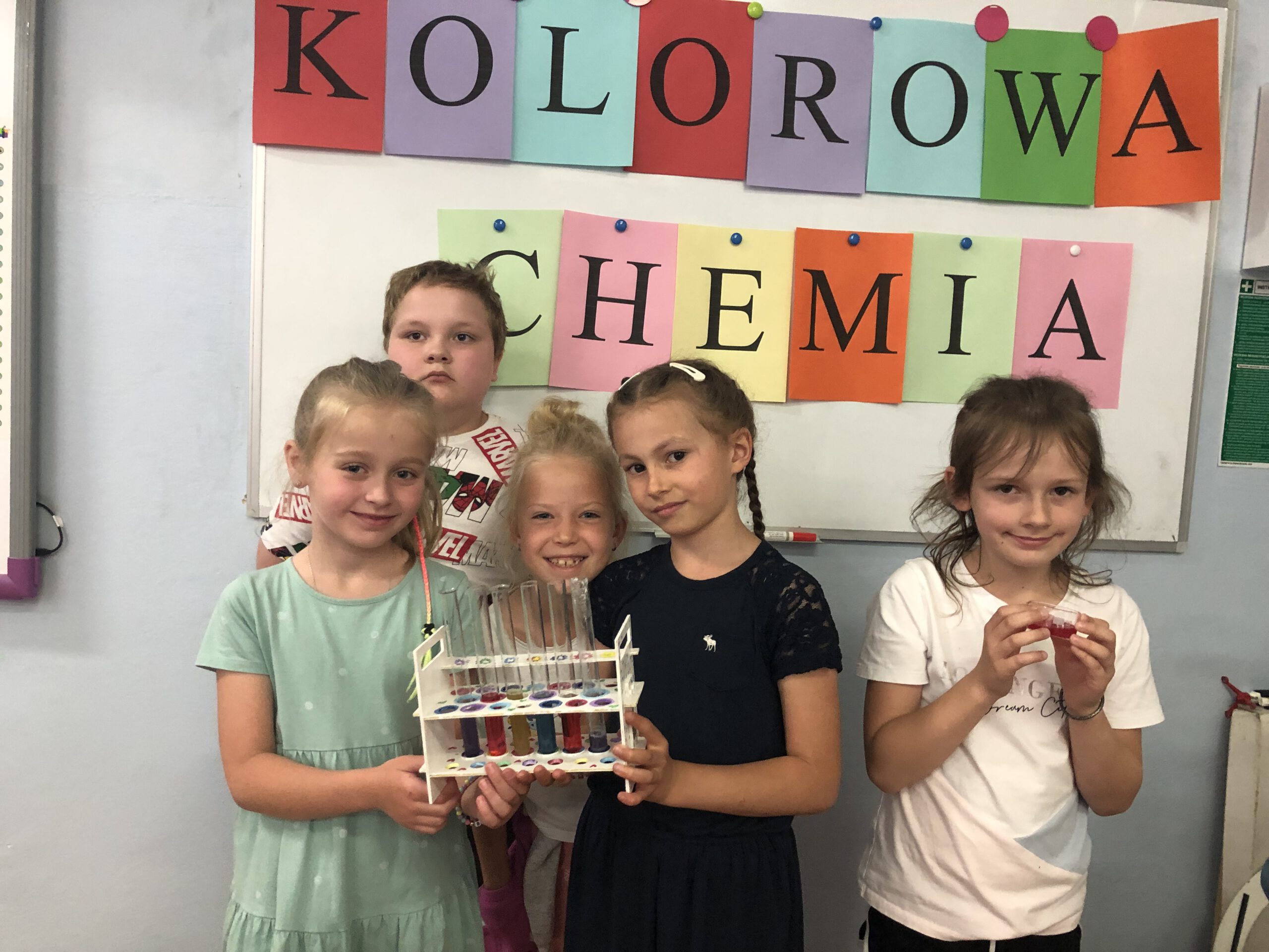 Chłopiec i cztery dziewczynki pozują do zdjęcia na tle napisu Kolorowa Chemia