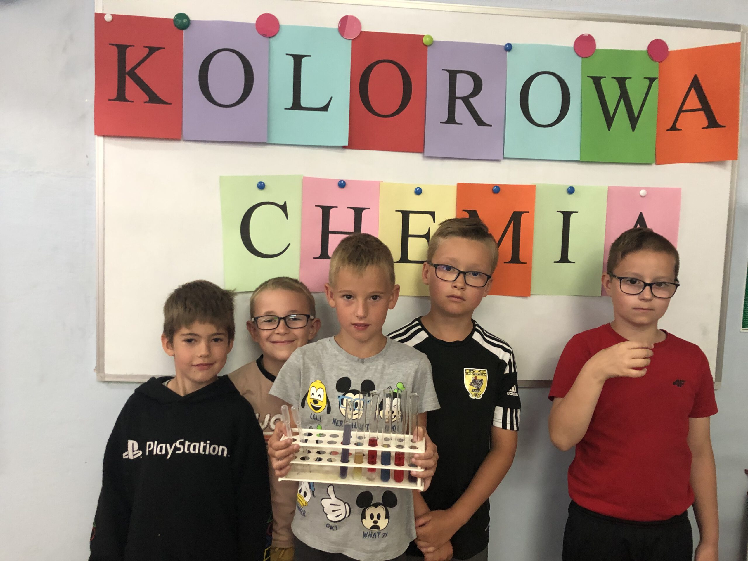 Pięciu chłopców pozuje do zdjęcia na tle napisu Kolorowa Chemia