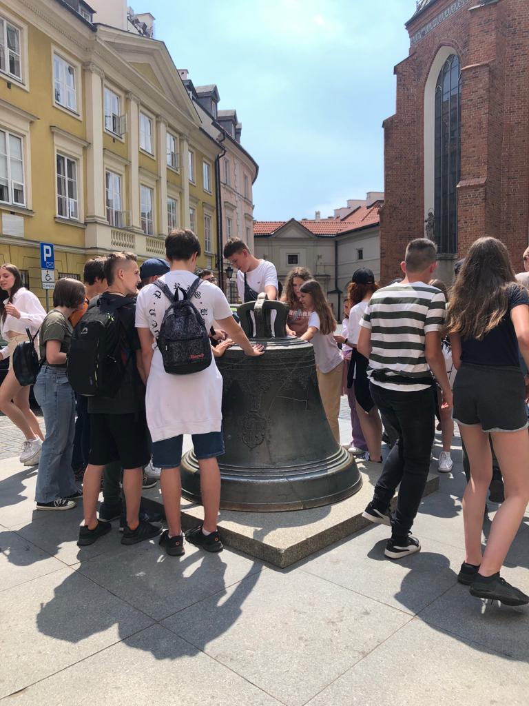 Uczniowie oglądają dzwon na chodniku warszawskiego rynku