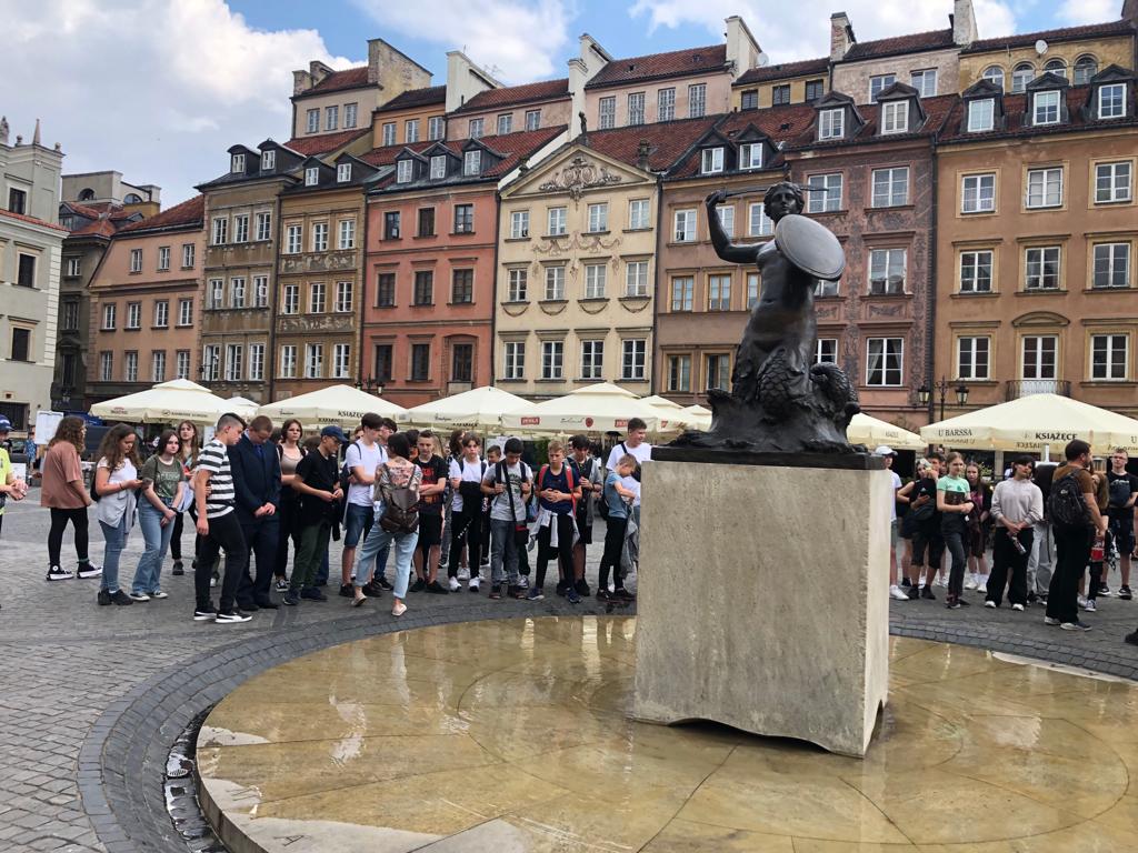 Grupa uczniów ogląda pomnik Syrenki warszawskiej