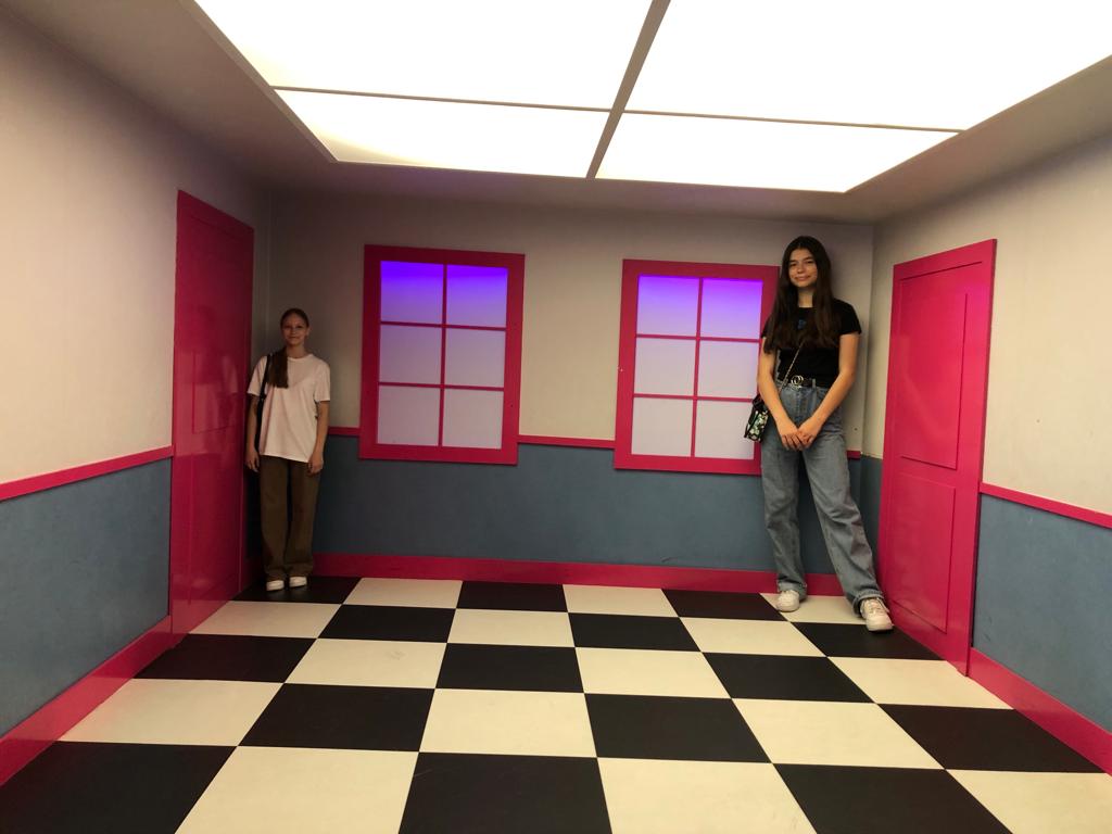 Dwie dziewczyny pozują do zdjęcia w pomieszczeniu zmieniającym proporcje wielkości
