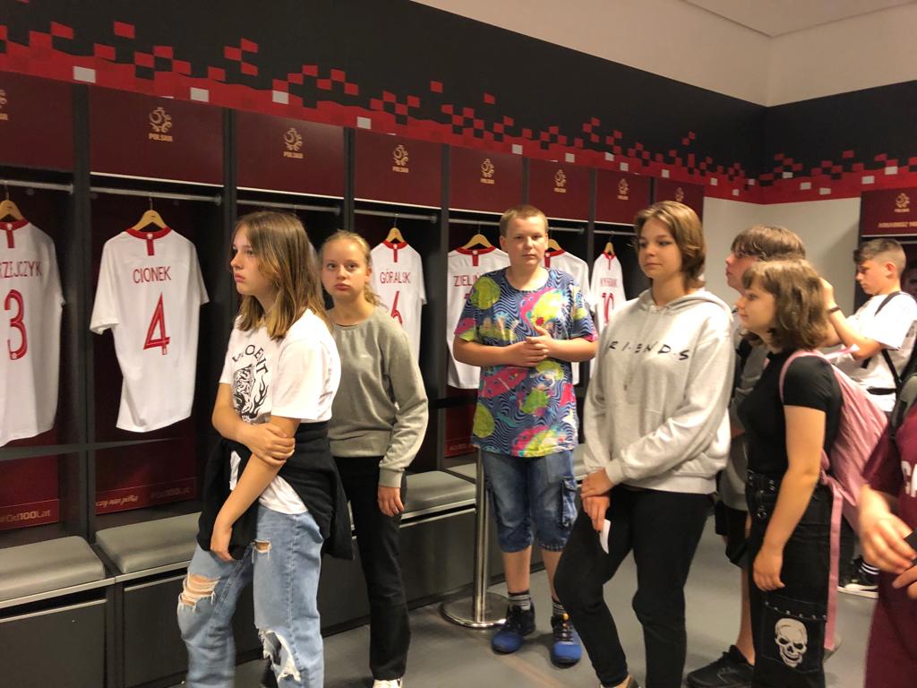 Grupa dziewcząt w szatni zawodników na tle koszulek reprezentacji Polski