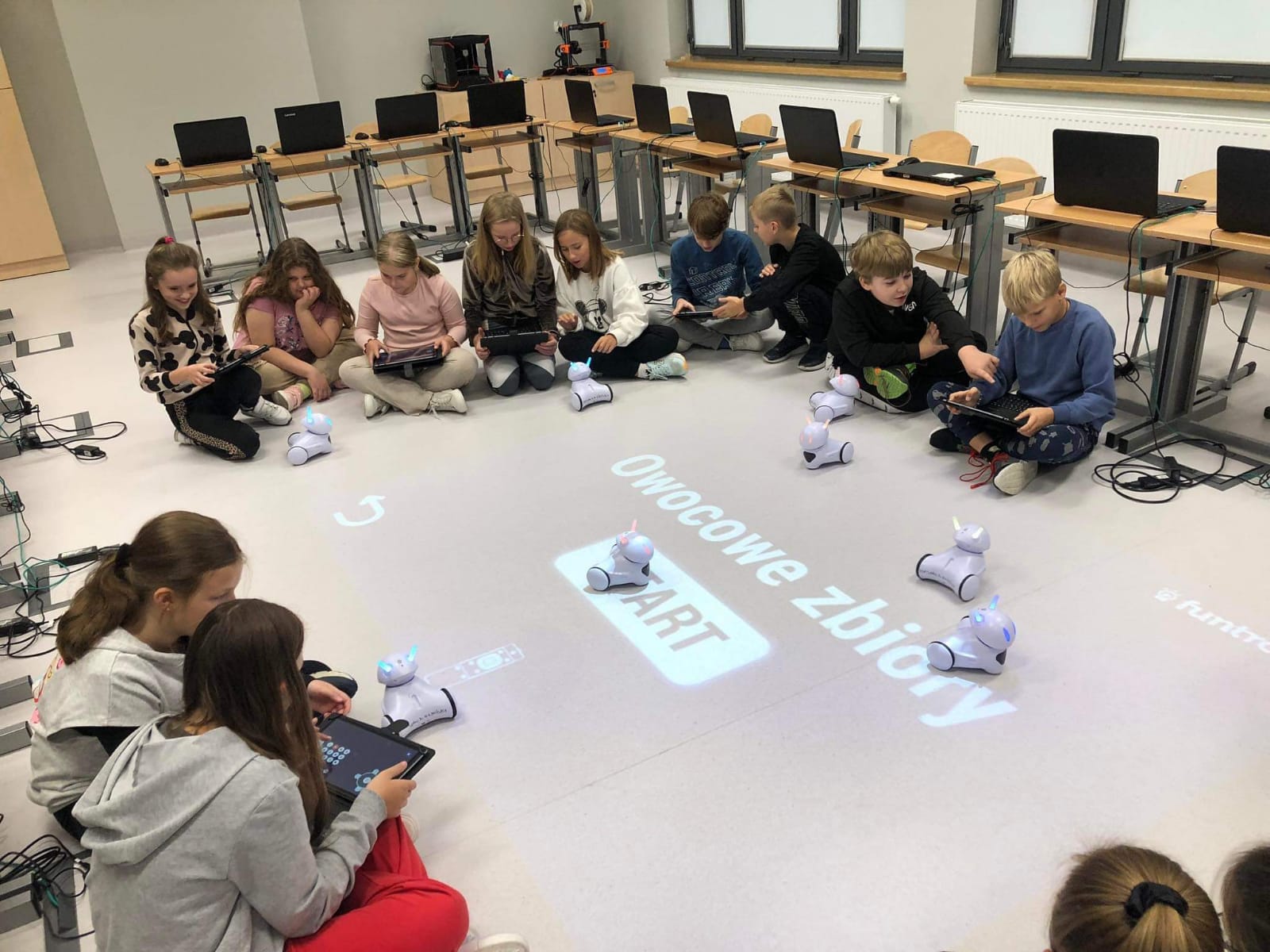 Grupa dzieci siedzi na podłodze i programuje roboty