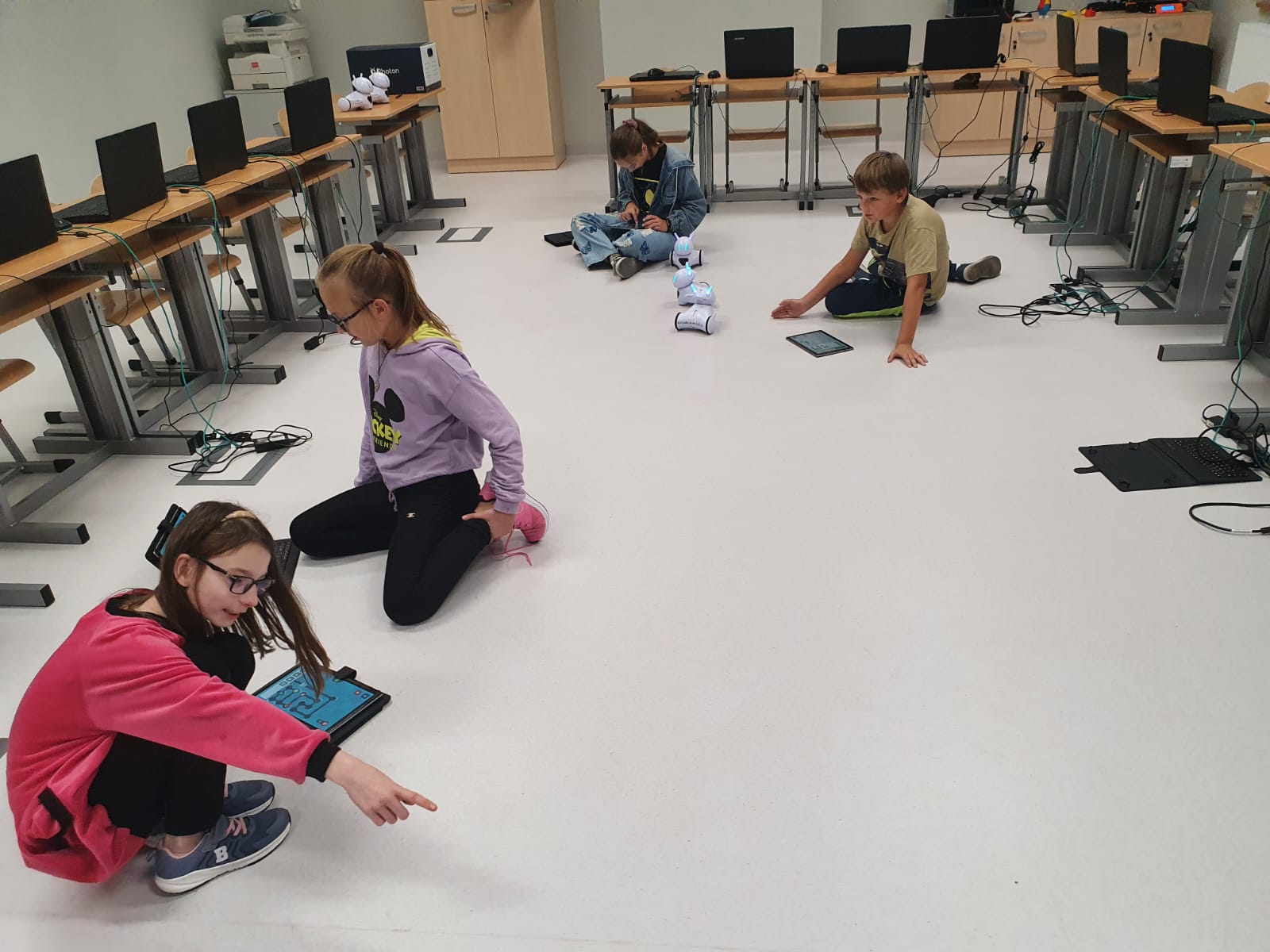 Czwórka uczniów kieruje zdalnymi robotami na podłodze sali lekcyjnej