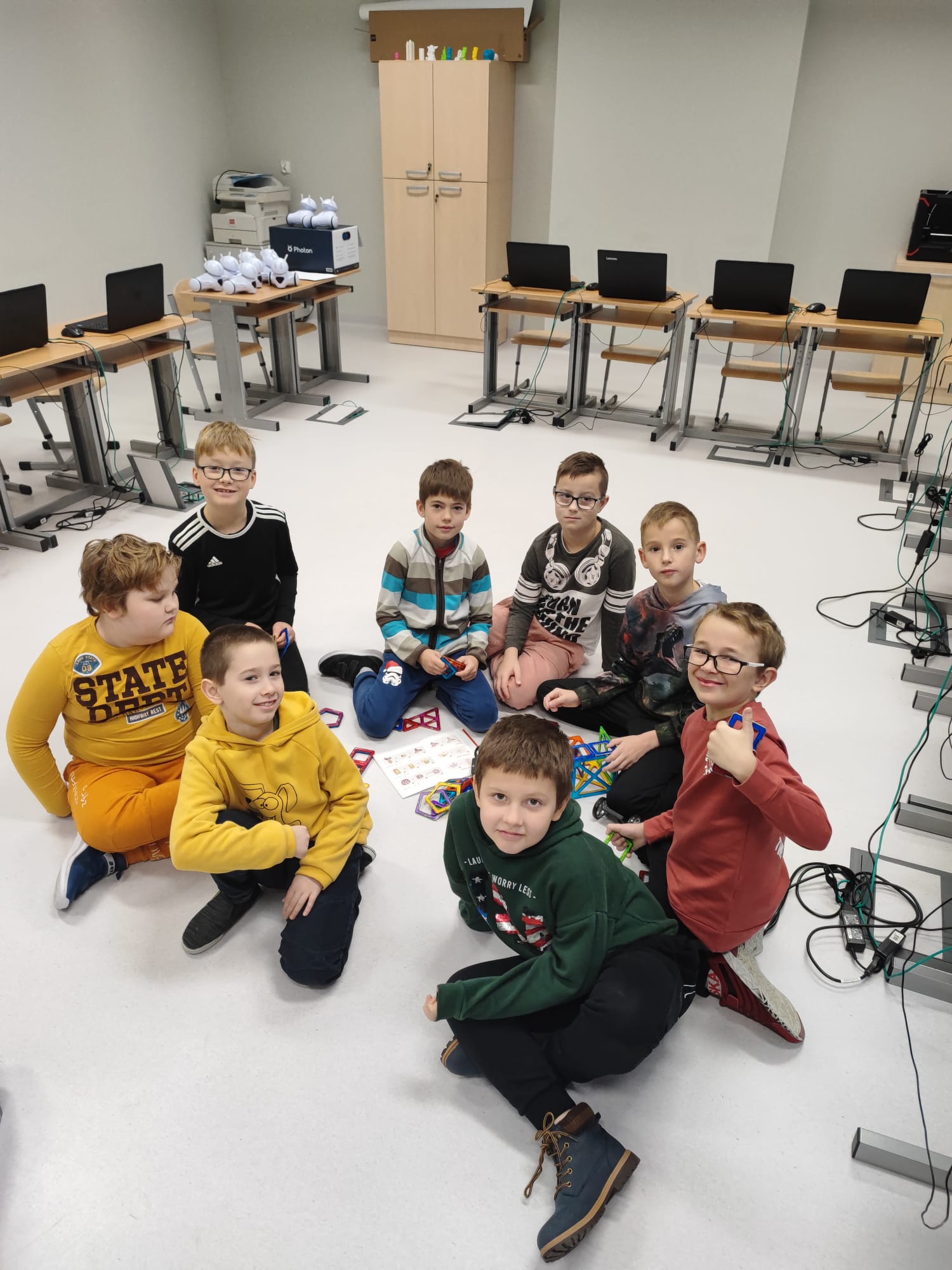 Ośmiu chłopców siedzi na podłodze i pozuje do zdjęcia na tle konstrukcji z klocków edukacyjnych