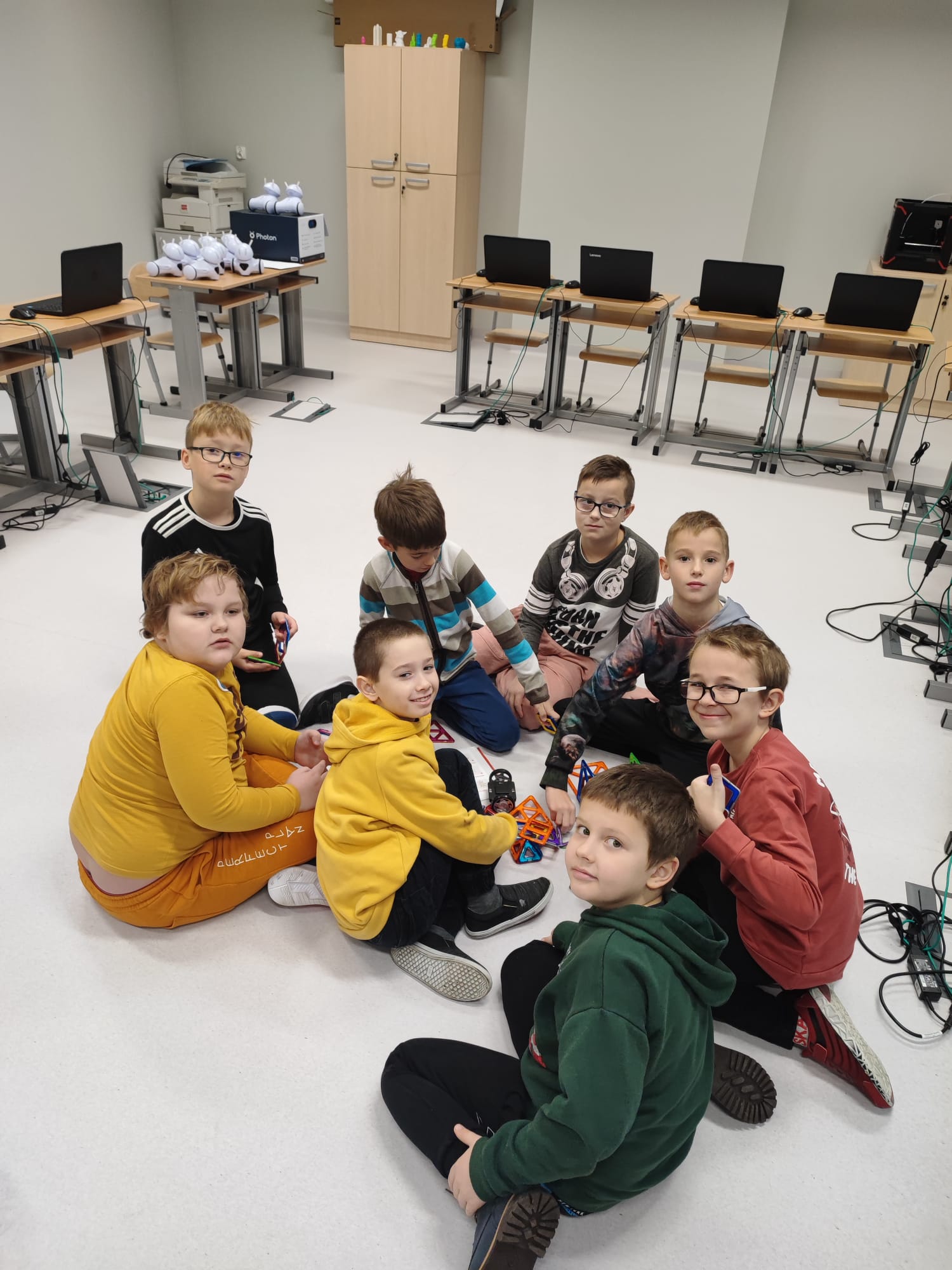 Grupa chłopców siedząc na podłodze układa konstrukcję z klocków