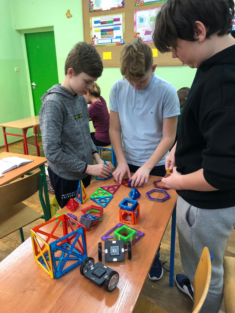Trzej chłopcy układają konstrukcję z plastikowych klocków